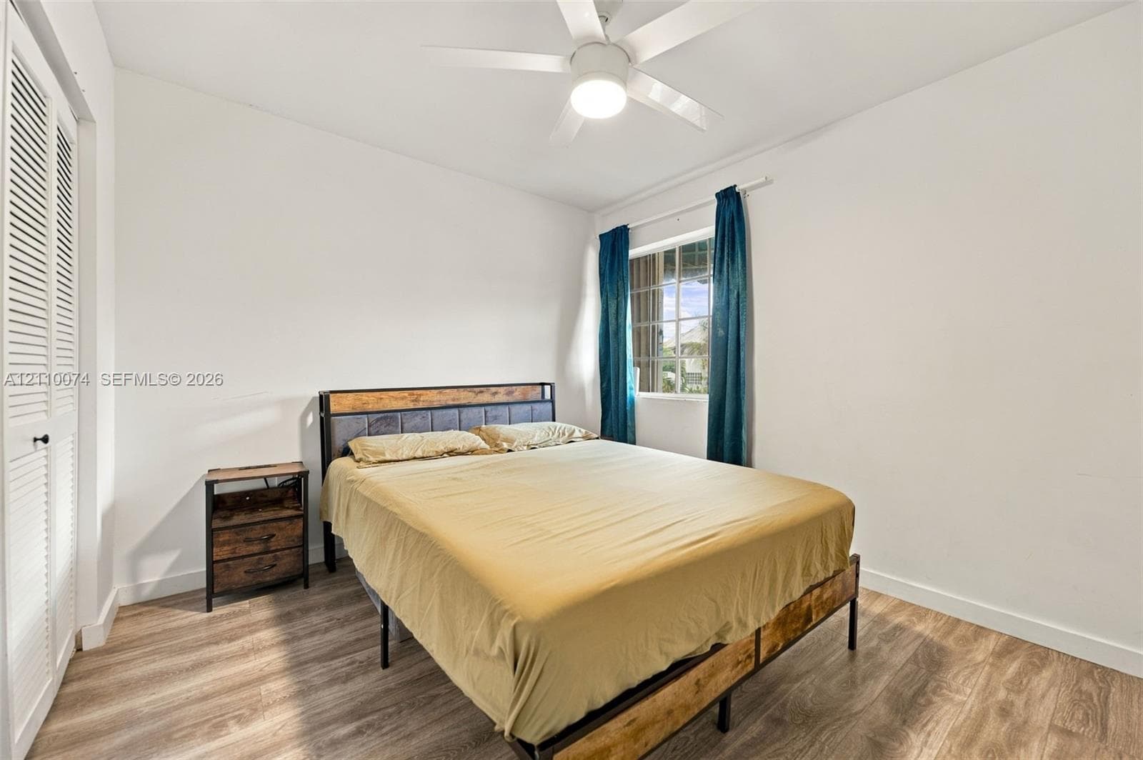 Bedroom featuring wood-finish flooring, a white ceiling fan with integrated lighting, and closet doors with louvered panels