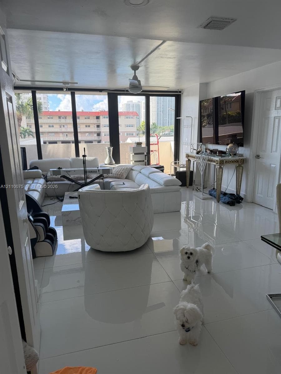 Open-concept interior featuring large-format polished tile flooring, expansive floor-to-ceiling windows, and a central ceiling fan