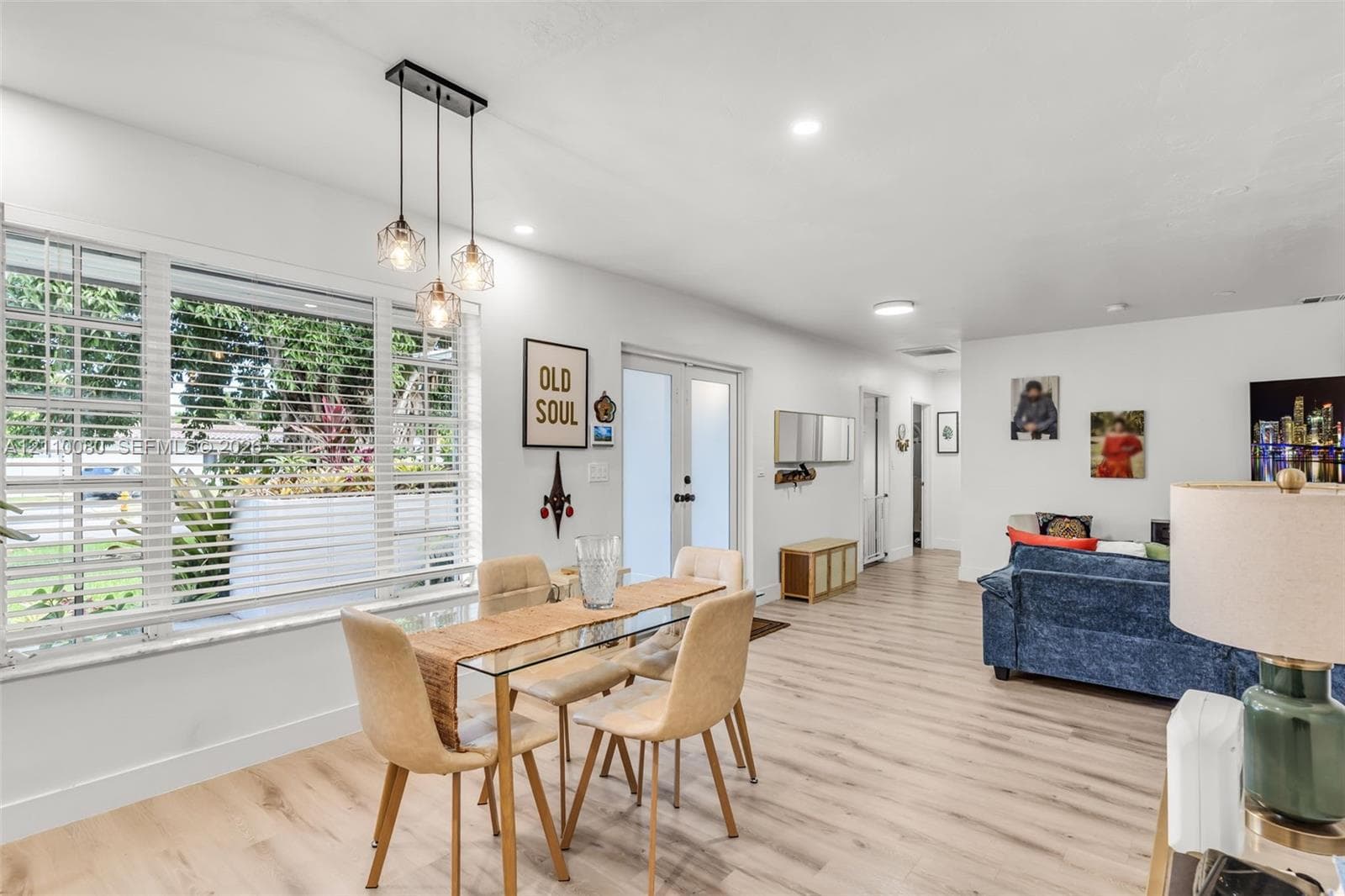 Wood-finish flooring, oversized picture window with horizontal blinds, three-light glass pendant fixture, and double glass-panel doors