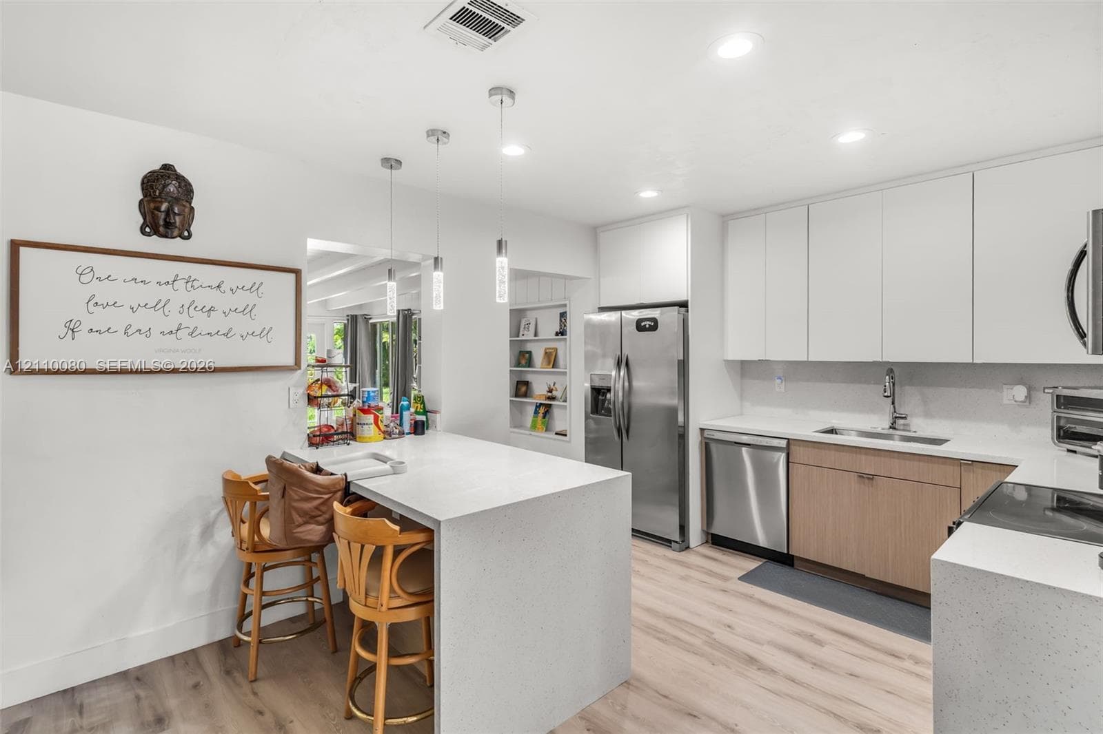 Kitchen featuring wood-finish flooring, white flat-panel upper cabinetry, waterfall-edge stone countertop, stainless steel appliances, and integrated pendant lighting