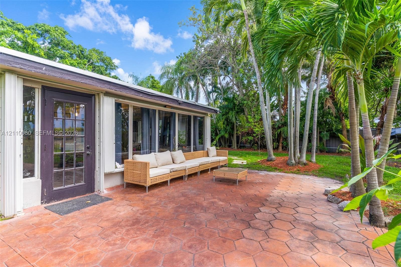Exterior patio featuring hexagonal terracotta-toned pavers, mature palm trees, and floor-to-ceiling windows