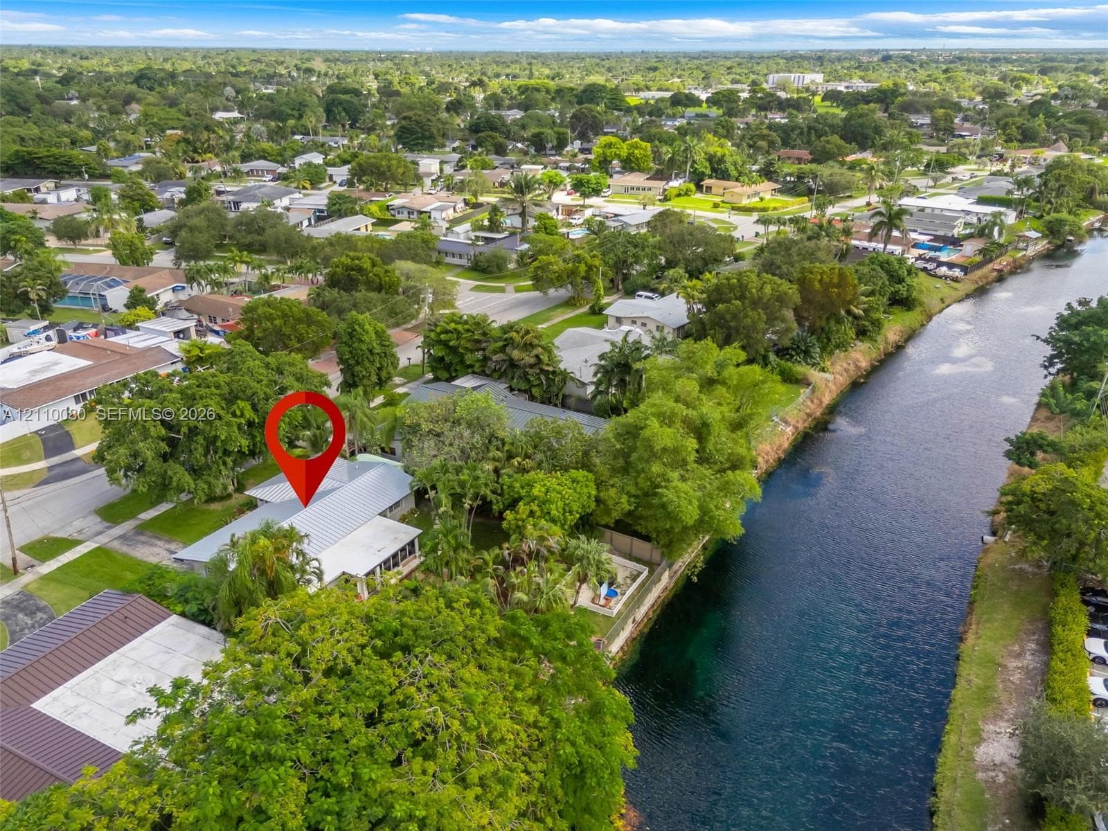 Aerial perspective of a waterfront property featuring direct canal frontage, a metal roof, screened-in porch, and mature landscaping
