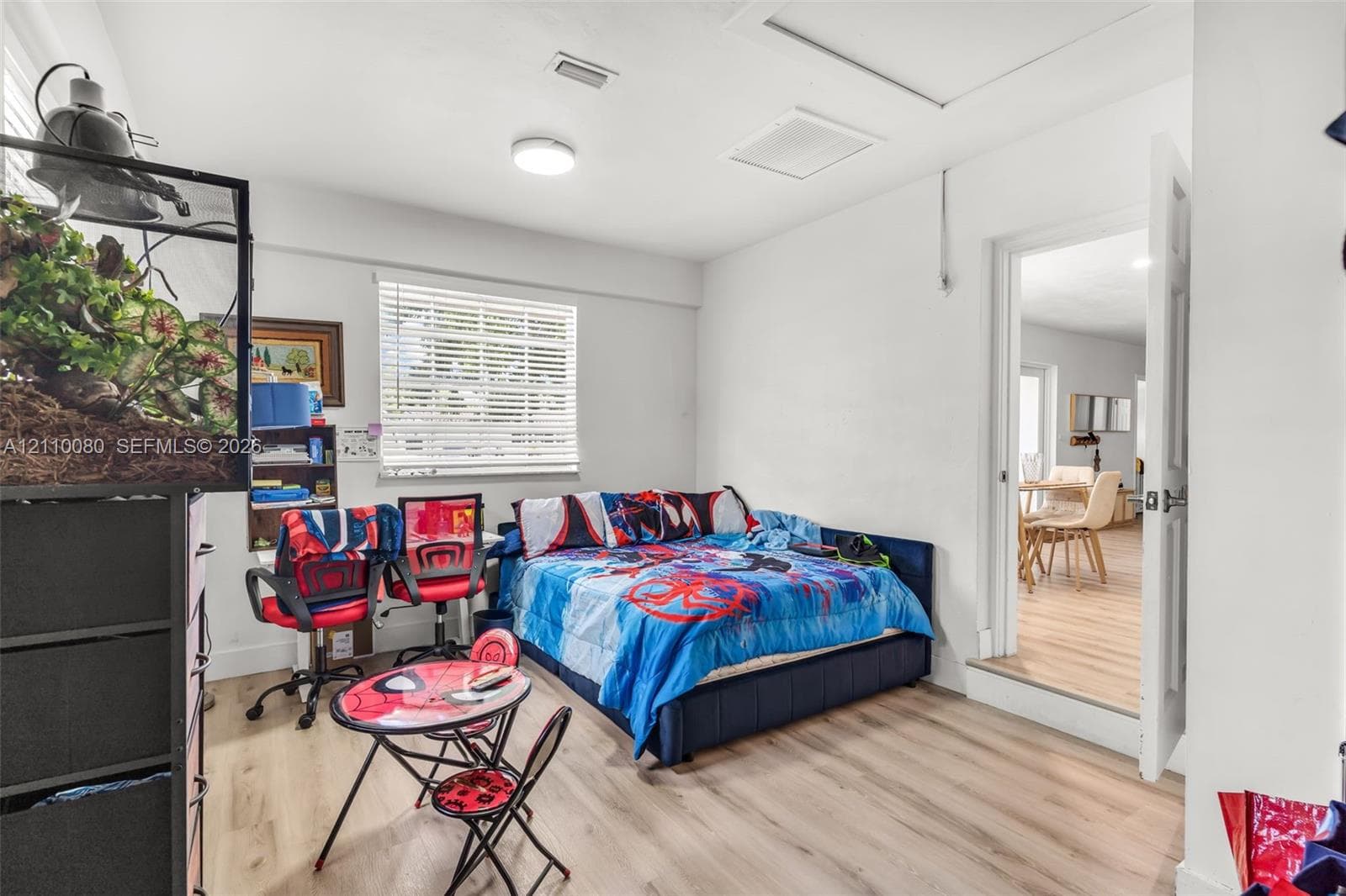 Room interior featuring wood-finish flooring, a horizontal window with slatted blinds, and a door opening to an additional space