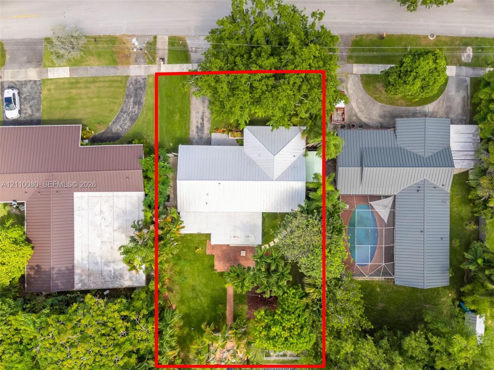 Aerial perspective of a property featuring a metal roof, paved driveway, brick patio, and mature landscaping