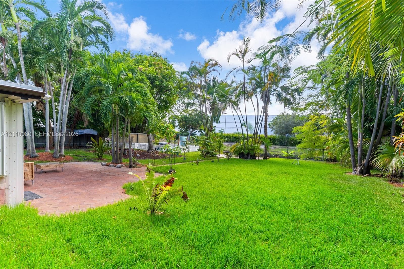 Landscaped backyard featuring a paved patio, mature palm trees, and perimeter fencing
