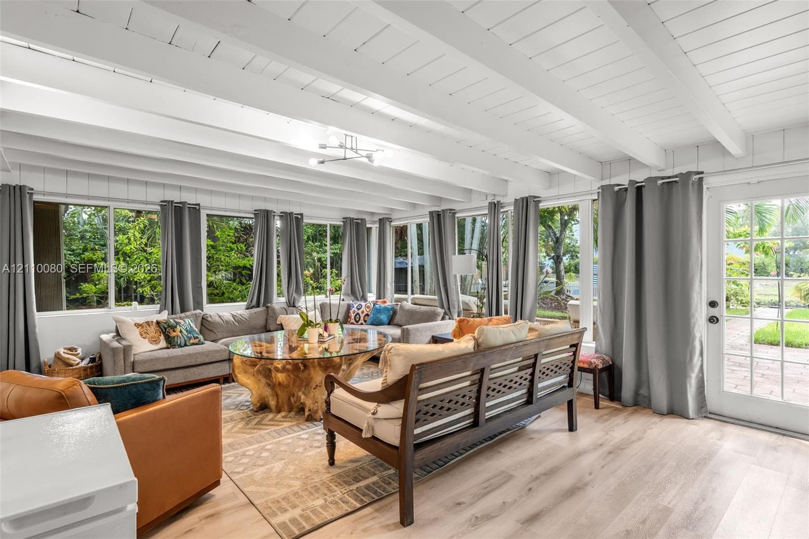 Sunroom featuring vaulted ceilings with exposed beams, wood-finish flooring, extensive floor-to-ceiling windows, and a glass-paned exterior door