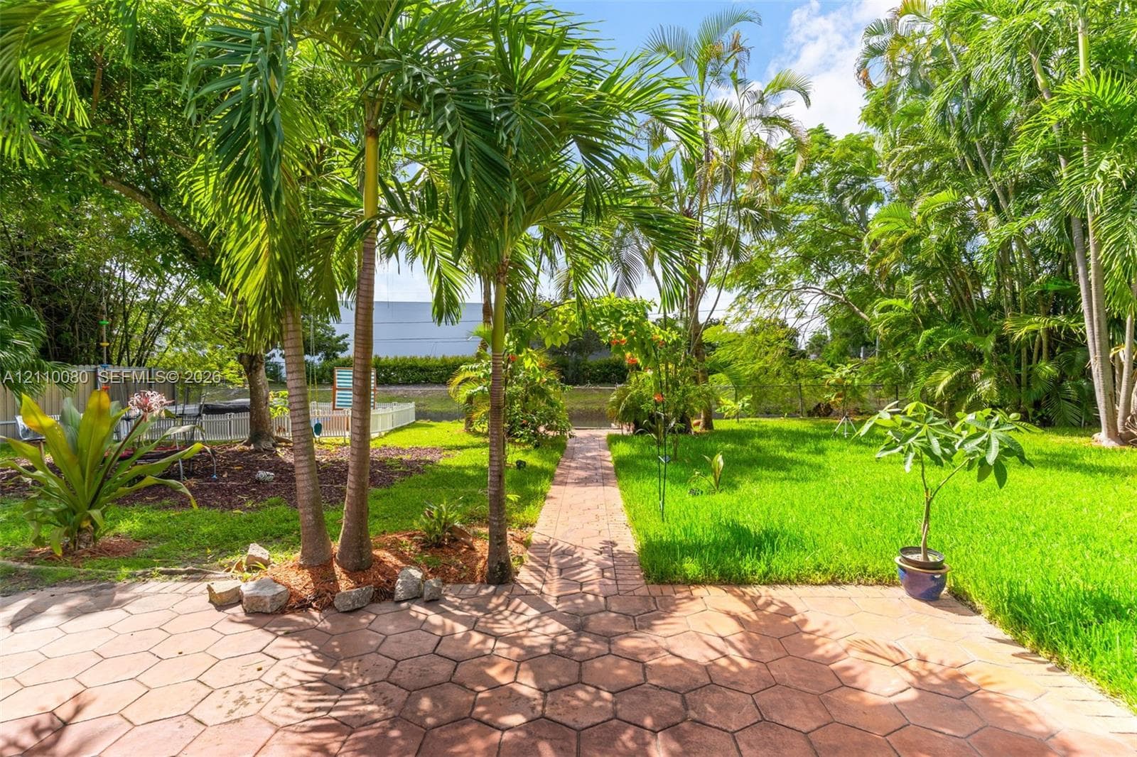 Rear yard featuring a hexagonal paver patio, a paver pathway, mature palm trees, and an open grass area
