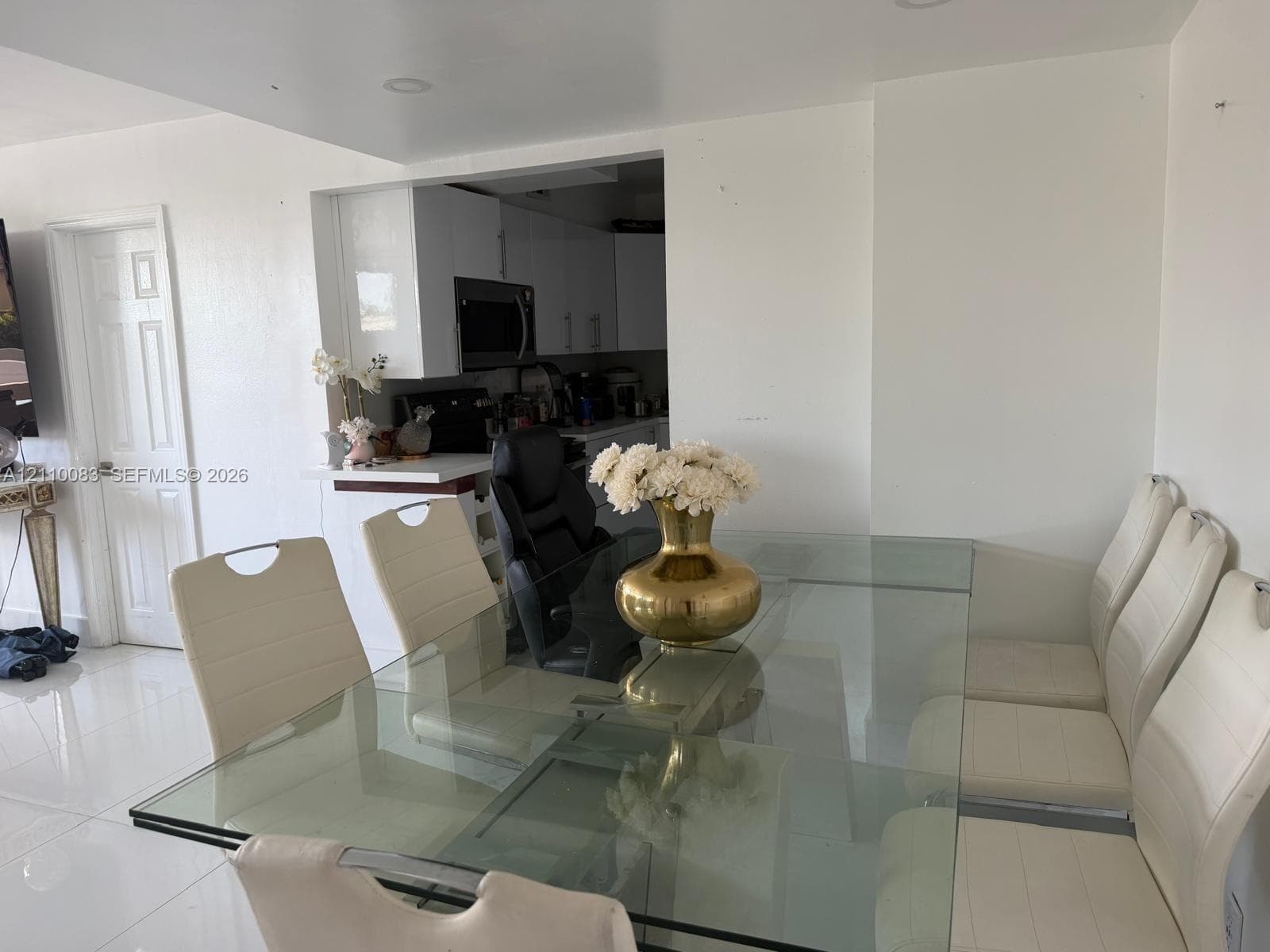Dining area featuring high-gloss tile flooring, recessed ceiling lighting, and a neutral color palette, opening to a kitchen equipped with white cabinetry and a built-in microwave