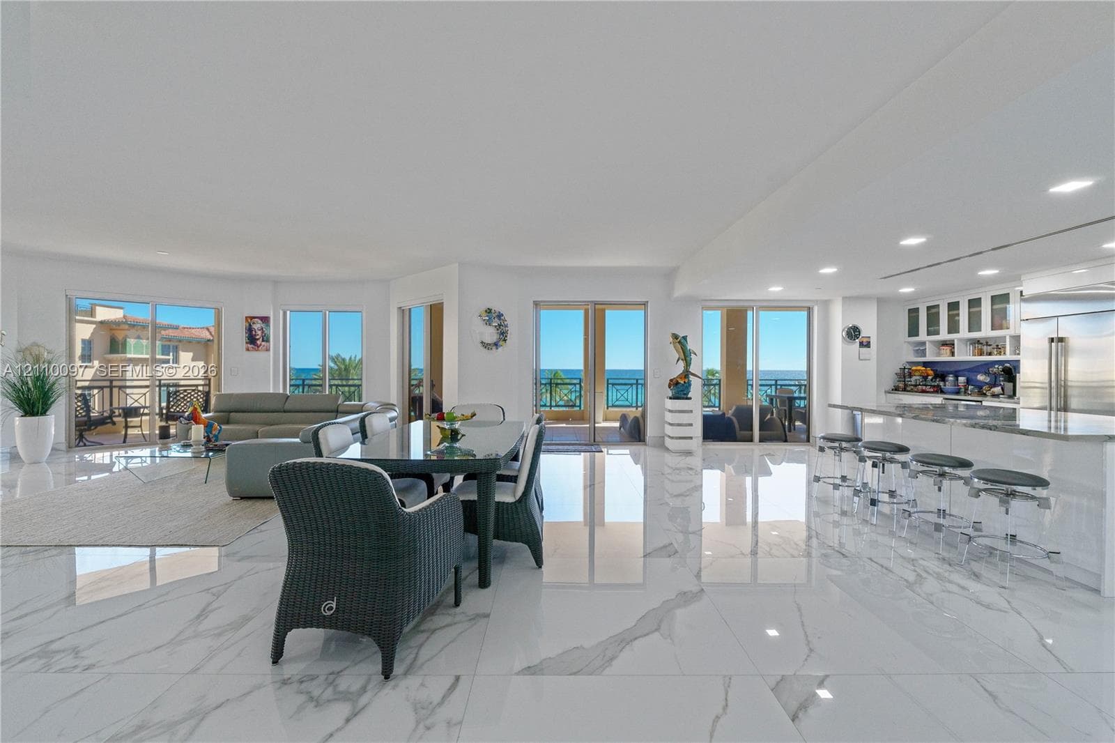 Open-concept living space featuring large-format polished tile flooring, a kitchen island with stone countertop, recessed lighting, and multiple sliding glass doors providing outdoor access