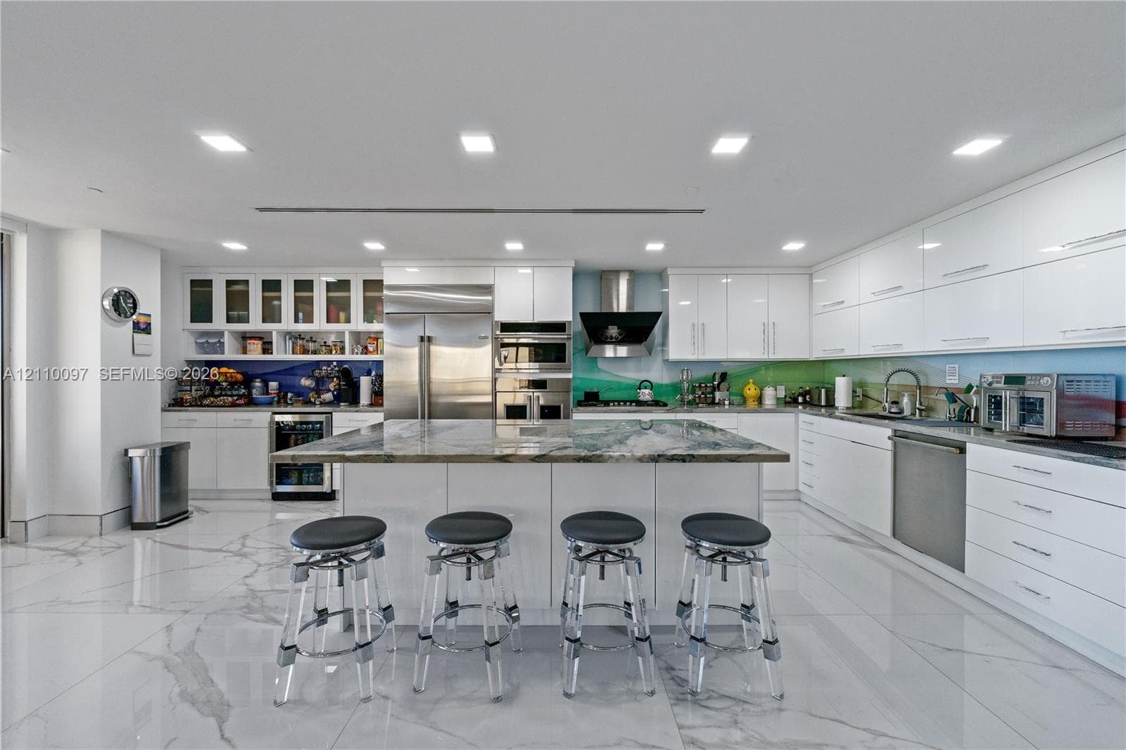 Modern kitchen featuring high-gloss cabinetry, a central island with natural stone countertop, stainless steel appliances, and large-format tile flooring