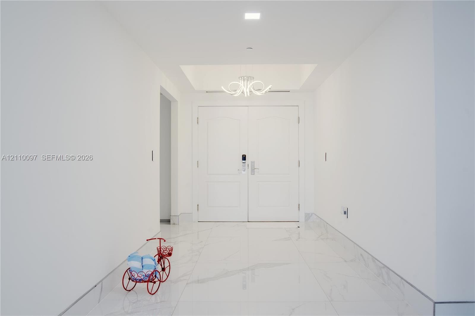 Entryway featuring double doors with a digital lock, large-format stone-patterned flooring, a recessed tray ceiling, and a multi-arm sculptural light fixture