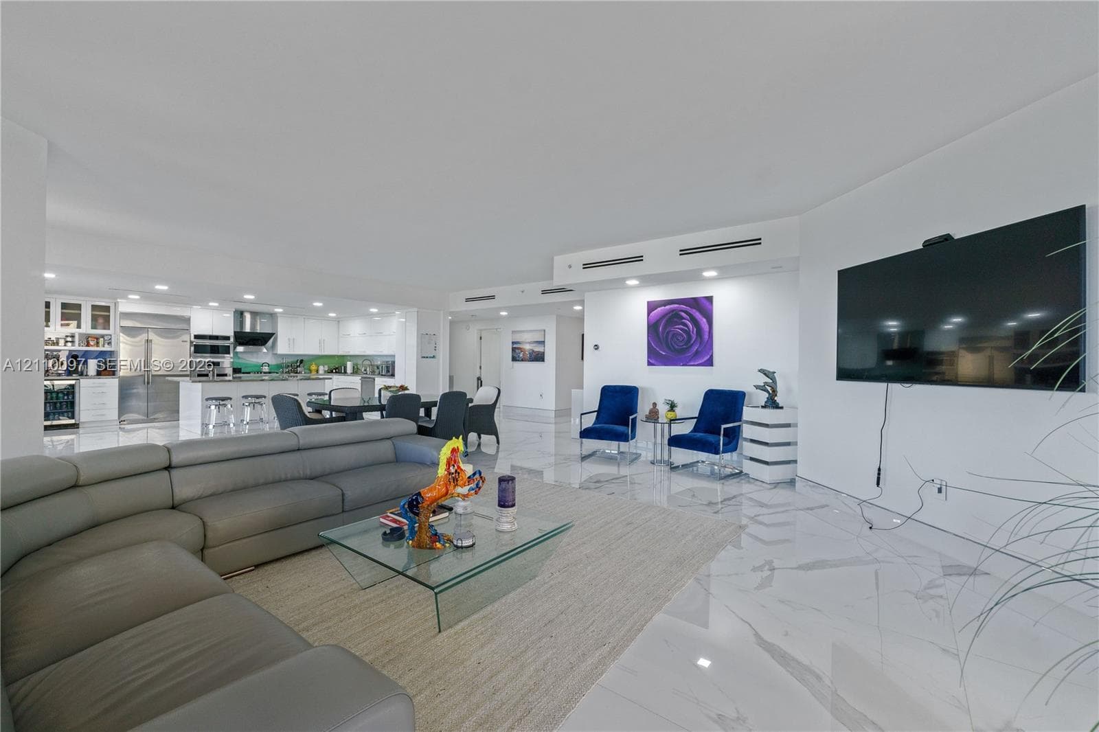 Open-concept living space featuring large-format stone-finish flooring, recessed lighting, white cabinetry, integrated stainless steel appliances, and a kitchen island with a breakfast bar