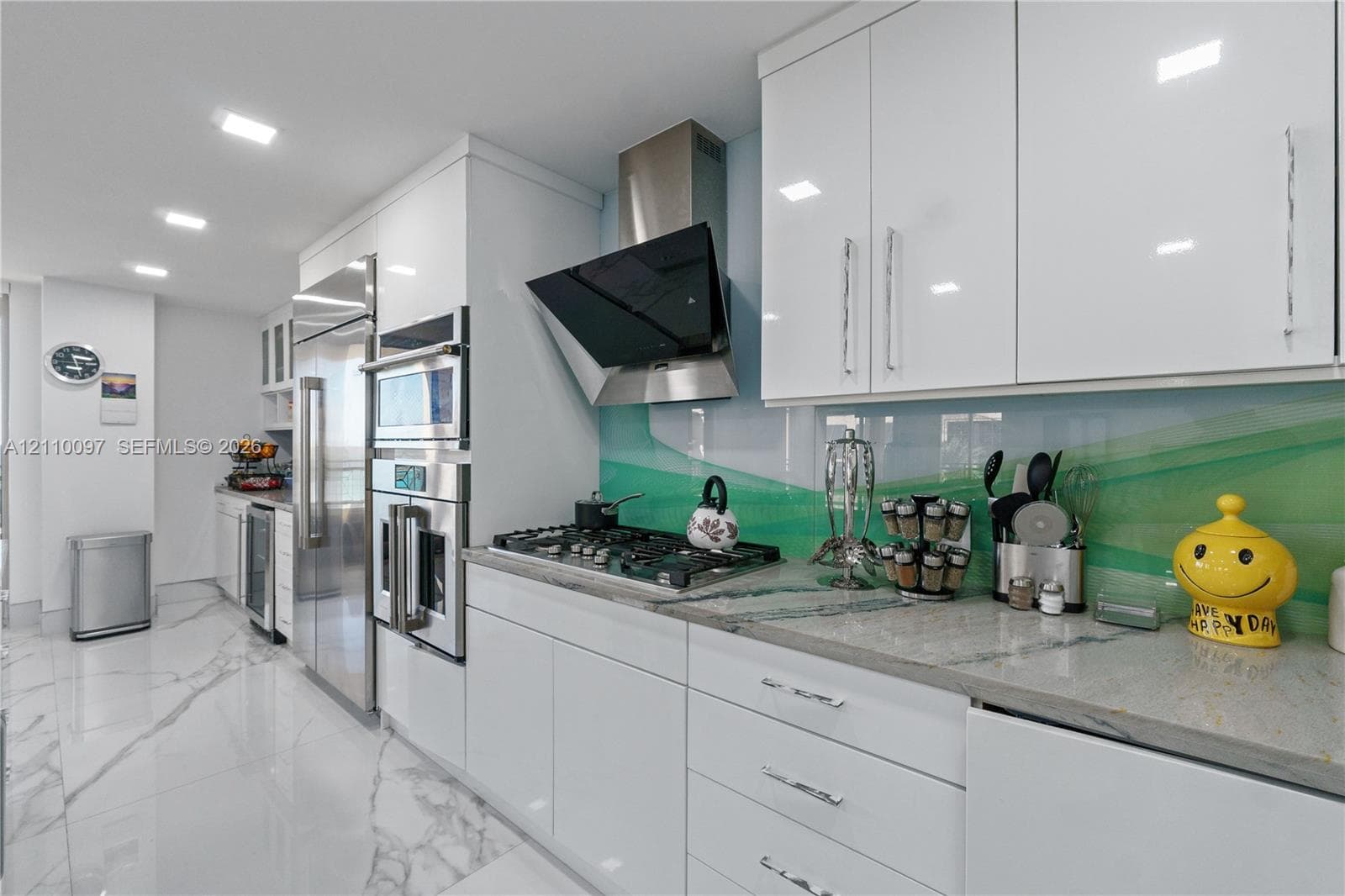 Contemporary kitchen featuring white high-gloss cabinetry, stone countertops, integrated stainless steel appliances, a gas cooktop with a wall-mounted range hood, and large-format porcelain tile flooring