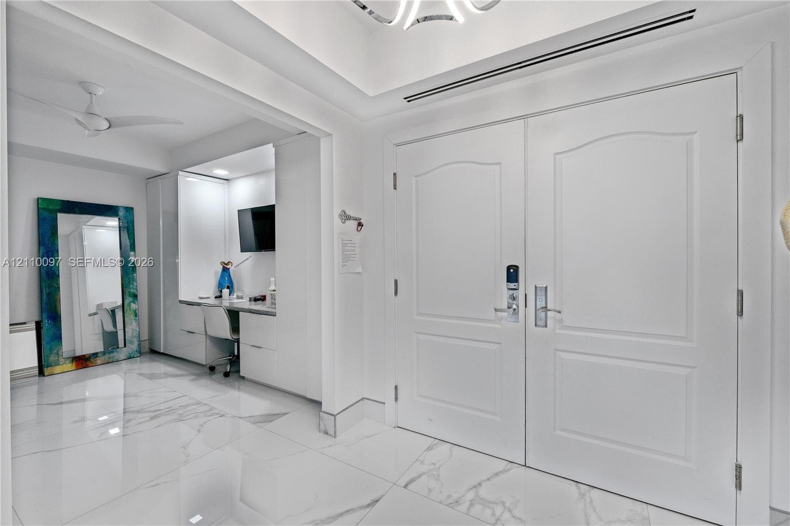 Double entry doors with arch-top panels, large-format tile flooring with marble-finish veining, recessed tray ceiling, and built-in cabinetry featuring integrated workspace