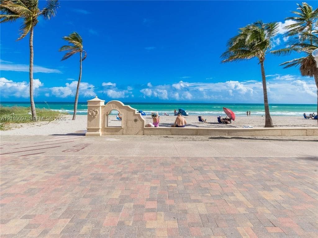 Brick-paver patio featuring a decorative stone archway, perimeter wall, and mature palm trees