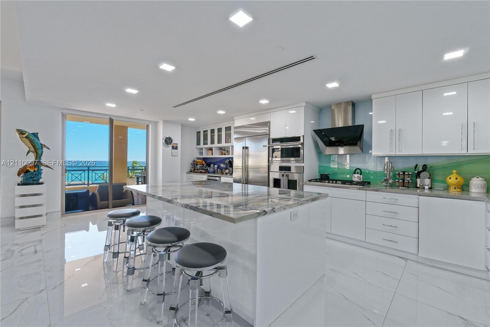 Modern kitchen featuring high-gloss cabinetry, a central island with natural stone surfacing, built-in stainless steel appliances, recessed lighting, and tile flooring
