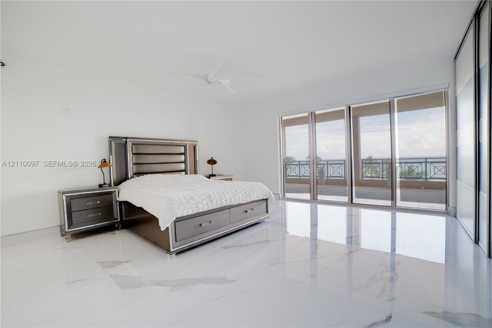 Polished stone flooring, floor-to-ceiling sliding glass doors, built-in closet with sliding panels, ceiling-mounted fan, and private covered balcony
