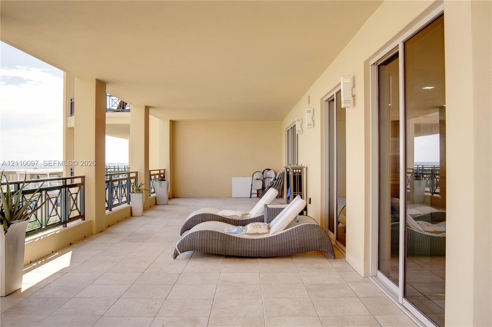 Covered balcony featuring neutral tile flooring, decorative metal railings, and multiple sliding glass door entries