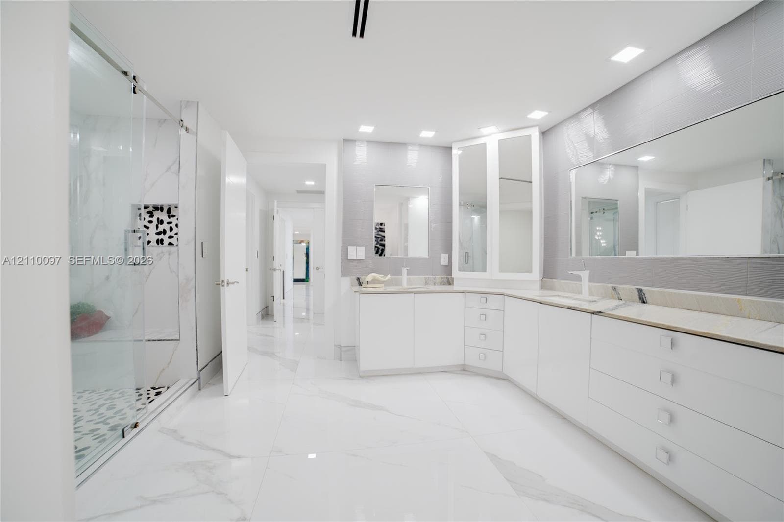 Large-format stone tile flooring, frameless glass shower enclosure, custom white cabinetry, stone-topped dual vanity, and recessed ceiling lighting