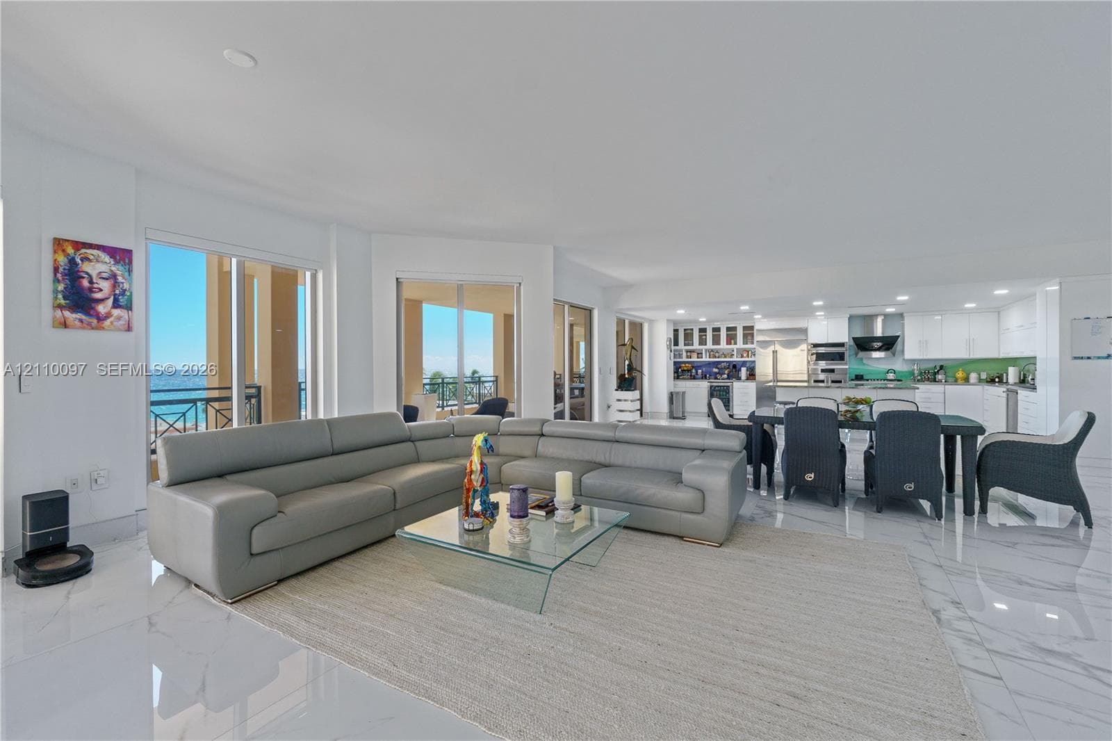 Open-concept floor plan with polished stone flooring throughout, expansive floor-to-ceiling glass sliding doors, and a gourmet kitchen featuring white cabinetry, professional-grade stainless steel appliances, and a central island
