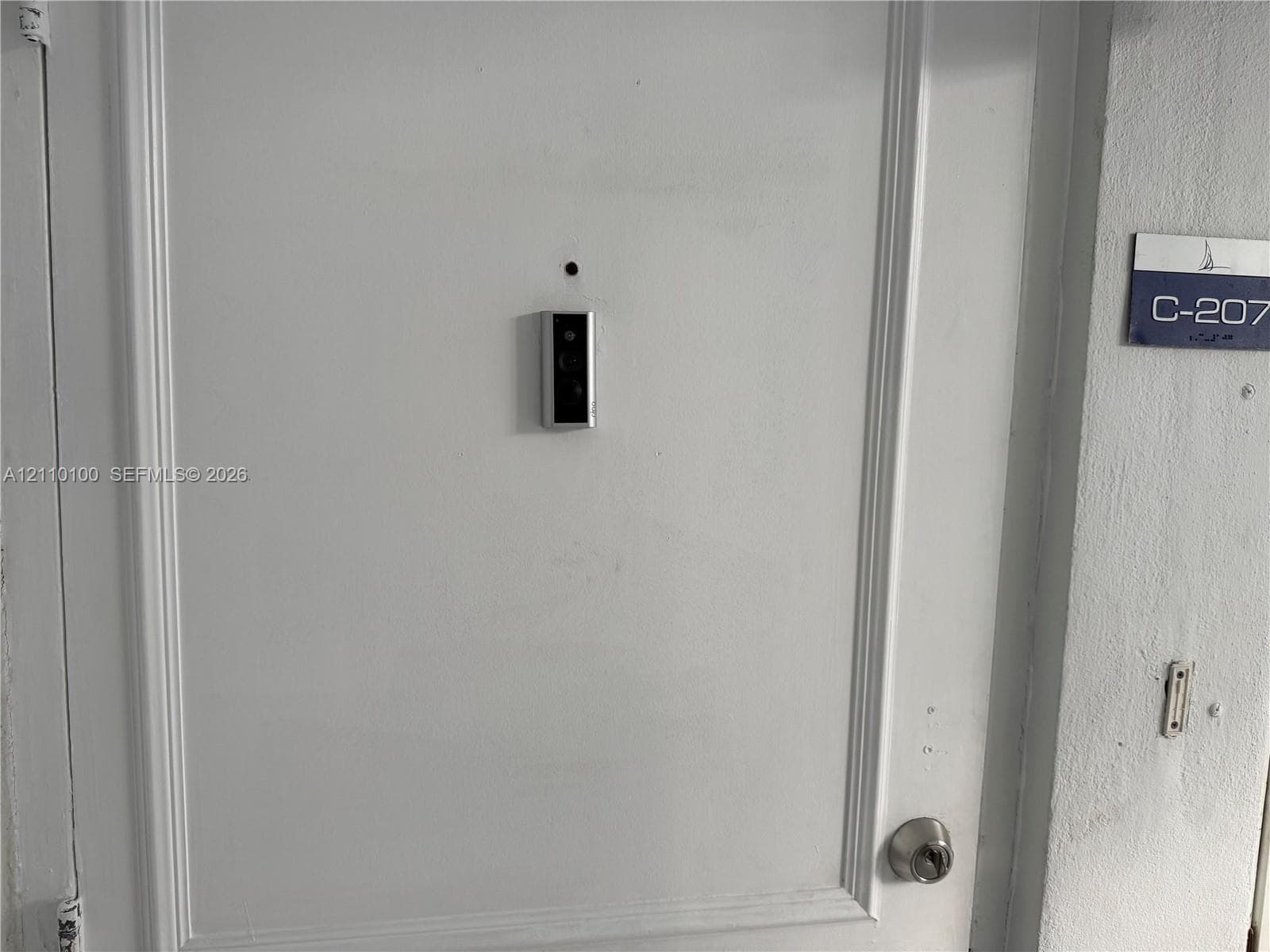 White paneled entry door equipped with a mounted smart doorbell and circular deadbolt lock