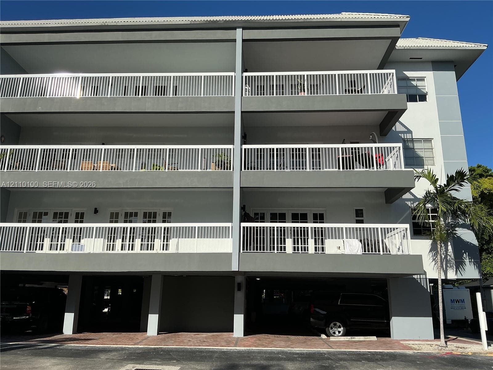 Multi-story exterior featuring multi-level balconies, white metal railings, French doors, and covered ground-level parking