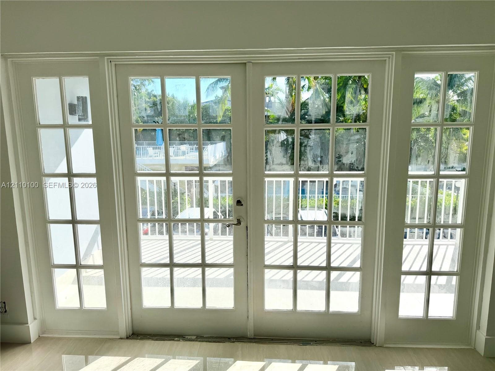 White French double doors with matching side lights and paneled glass, featuring metallic hardware and light-toned flooring