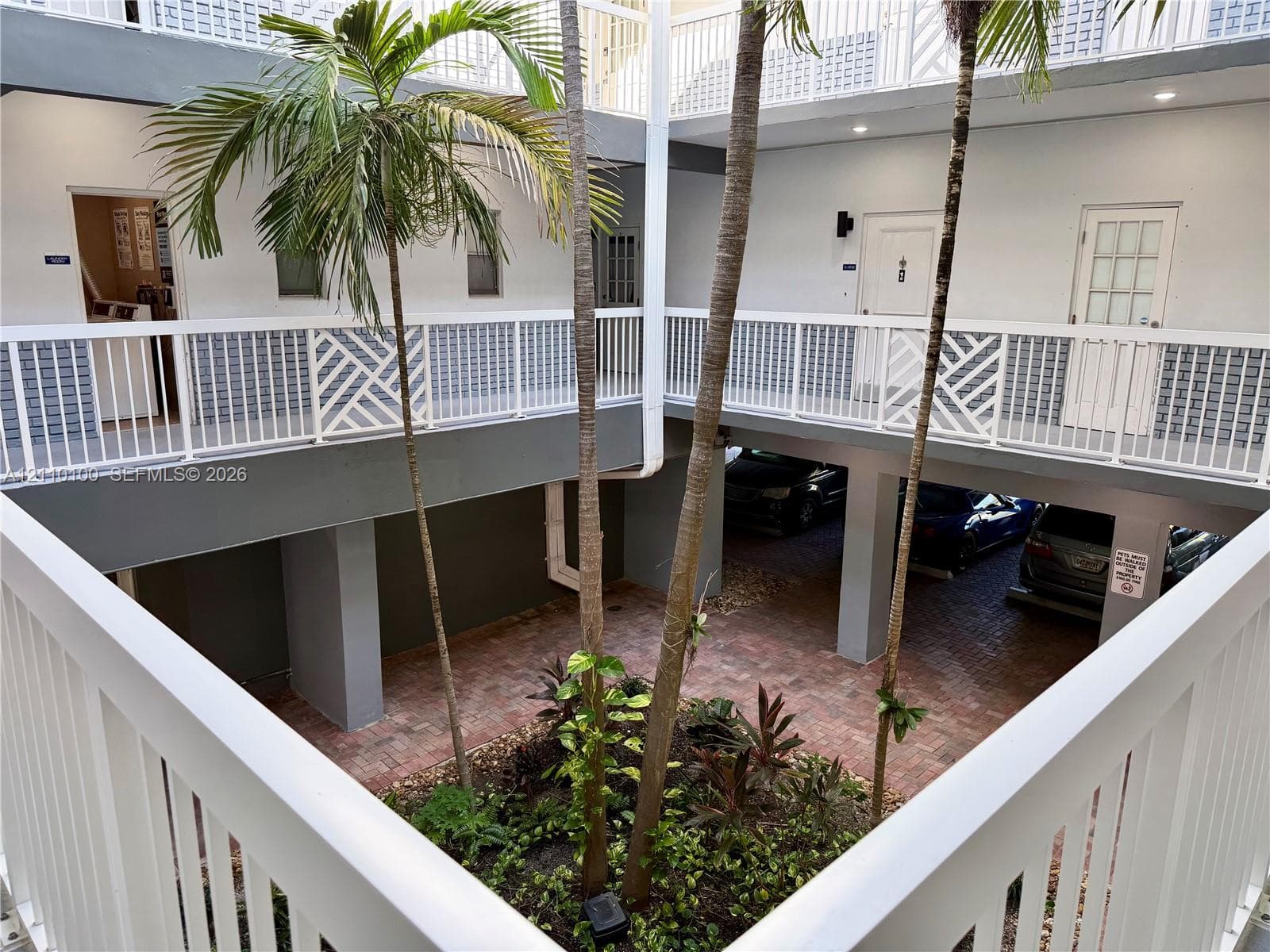 Central courtyard featuring brick pavers, mature palm trees, multi-level exterior walkways with white railings, and covered ground-level parking