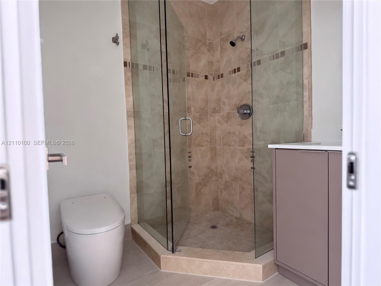 Corner shower enclosure with glass doors, neutral tile surround, accent tile inlay, and integrated vanity featuring a light-toned countertop