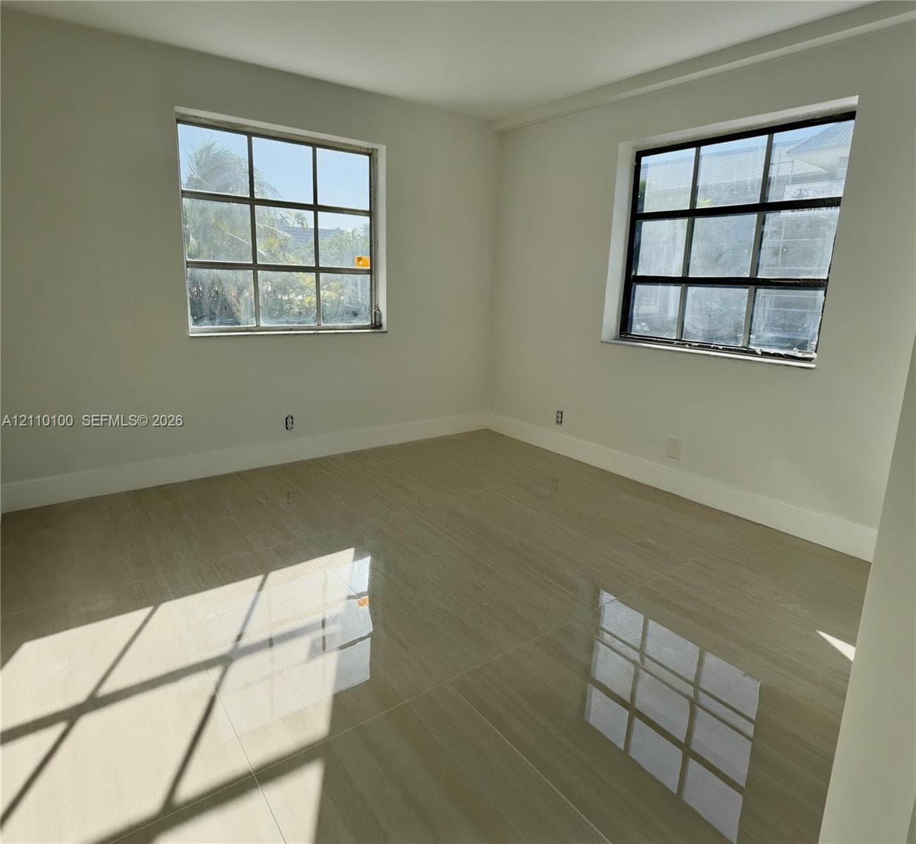 Room interior featuring large-format polished tile flooring, neutral wall tones, and two windows with multi-pane grid detailing