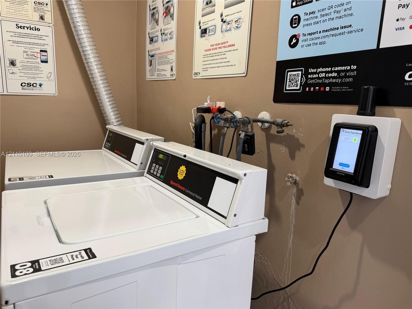 Commercial-grade top-load washing machines featuring digital payment terminals and integrated wall-mounted service interfaces