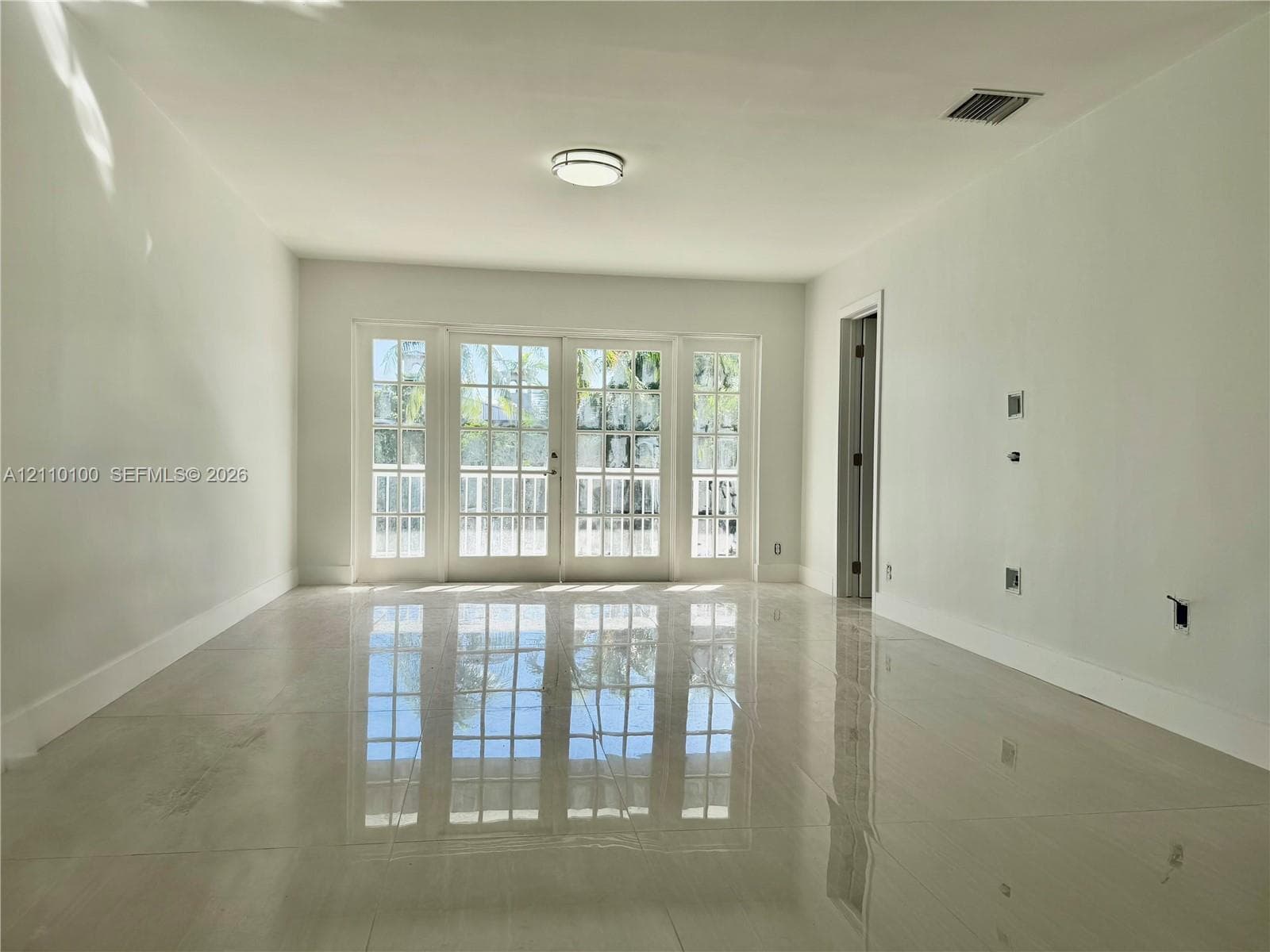 Interior space featuring polished tile flooring, white wall finishes, flush-mount ceiling lighting, and a multi-pane glass-panel door system