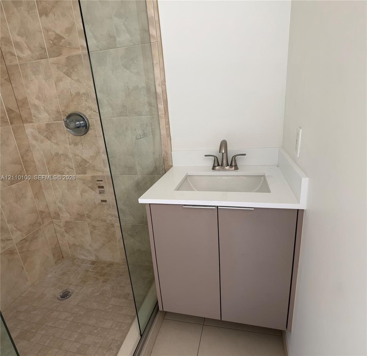 Floating vanity with a light-toned solid surface countertop, undermount sink, brushed nickel faucet, and a walk-in shower featuring glass enclosure and full-height stone-finish wall tile