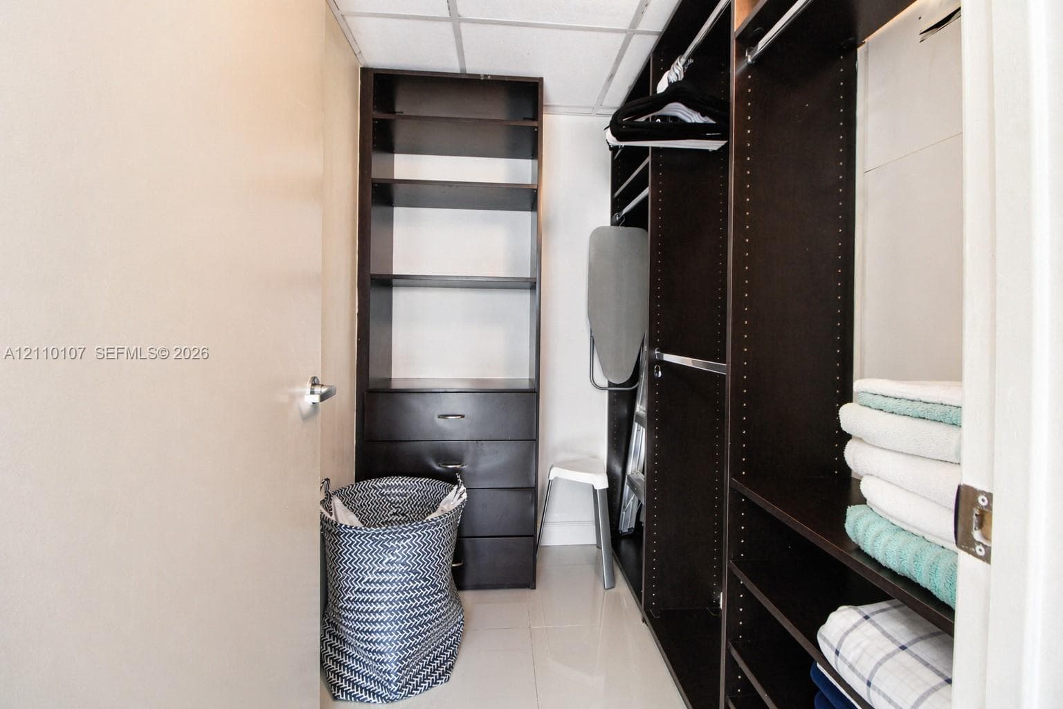 Walk-in closet featuring dark wood-finish built-in shelving, integrated dresser drawers, and dual hanging rods