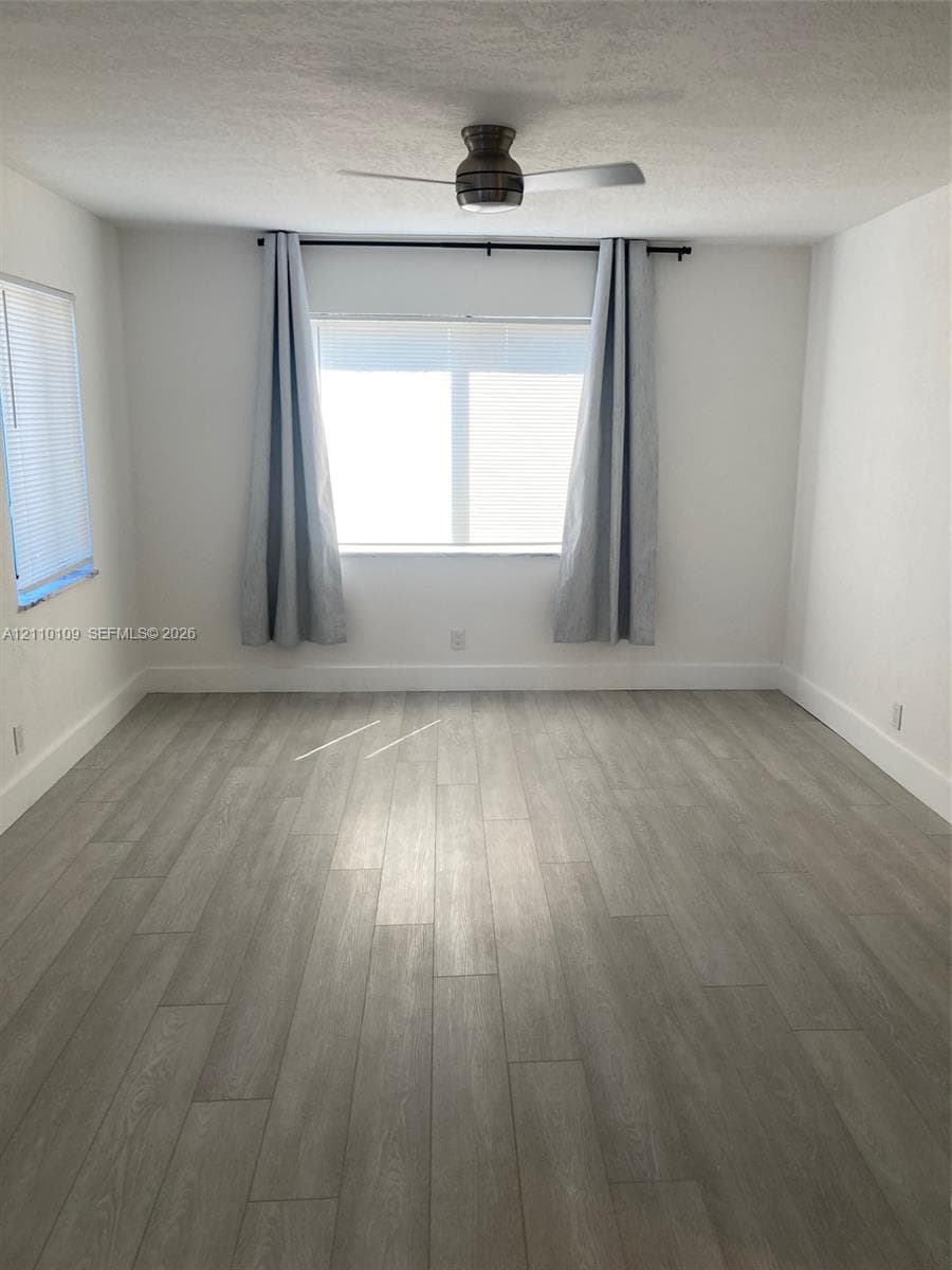 Neutral-toned interior space featuring wood-finish flooring, dual windows, and a ceiling-mounted fan