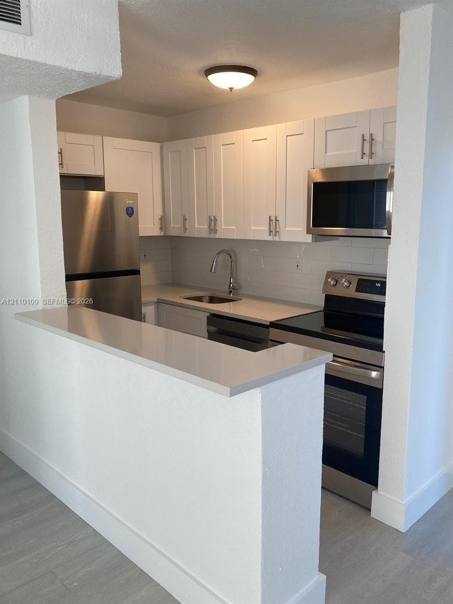 Kitchen featuring white cabinetry, quartz countertops, stainless steel appliances, a subway tile backsplash, and a breakfast bar