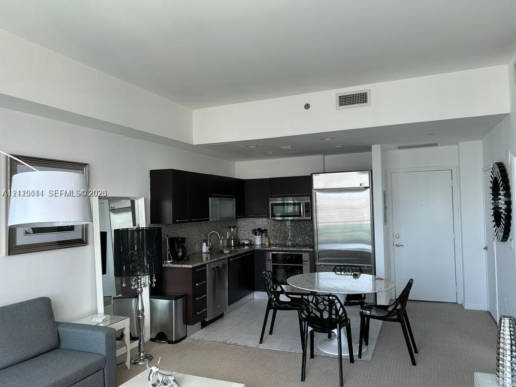 Kitchen featuring dark-finish cabinetry, stainless steel appliances, stone-finish countertops, and tile flooring