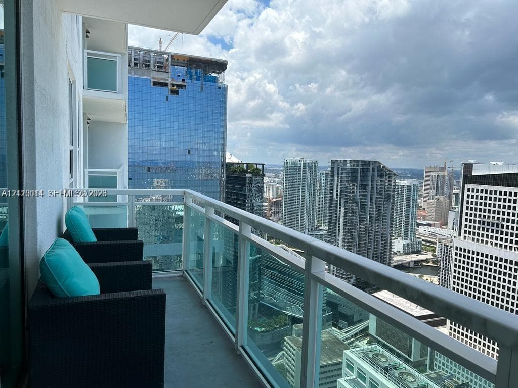 Private balcony featuring a glass-panel railing and concrete flooring, overlooking an urban cityscape