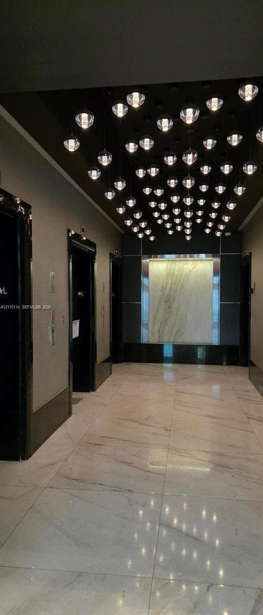 Grand lobby featuring large-format polished stone flooring, custom multi-pendant ceiling lighting, stone wall accent paneling, and high-gloss door frames