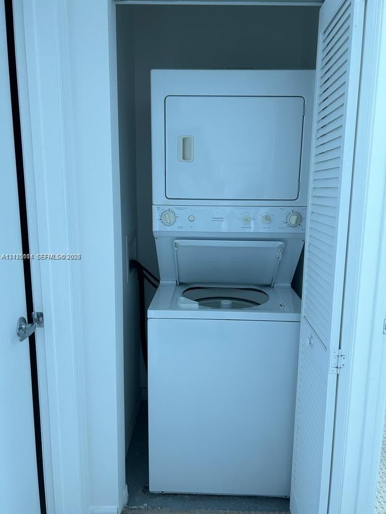 Stacked washer and dryer unit housed within a closet featuring white louvered doors