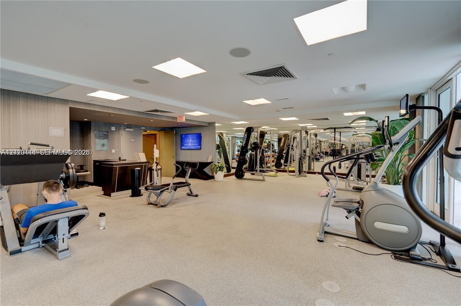 Fitness center featuring neutral carpeting, recessed lighting, expansive wall mirrors, and built-in reception cabinetry