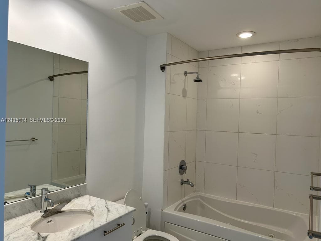 Bathroom featuring a vanity with a light-toned stone countertop, integrated sink, wall-mounted mirror, tub-shower combination with full-height tile surround, and metallic hardware