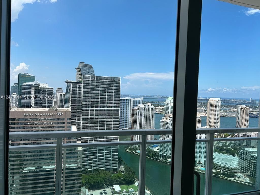 Floor-to-ceiling glass windows and a glass-paneled balcony railing showcasing a cityscape and waterfront horizon