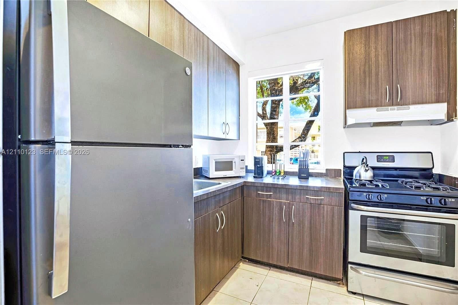 Kitchen featuring wood-finish cabinetry, stainless steel appliances, dark countertops, and tile flooring