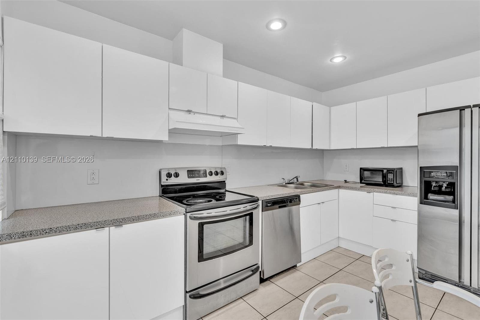 Kitchen featuring white flat-panel cabinetry, speckled stone-finish countertops, stainless steel appliances, and tiled flooring