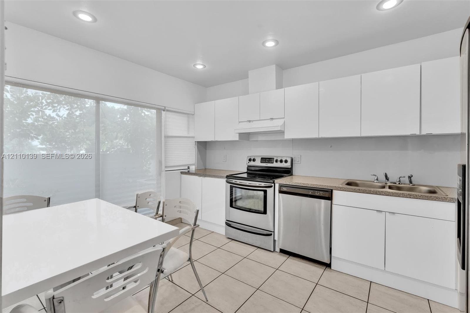 Kitchen featuring white flat-panel cabinetry, stainless steel appliances, neutral countertops, tile flooring, and recessed lighting