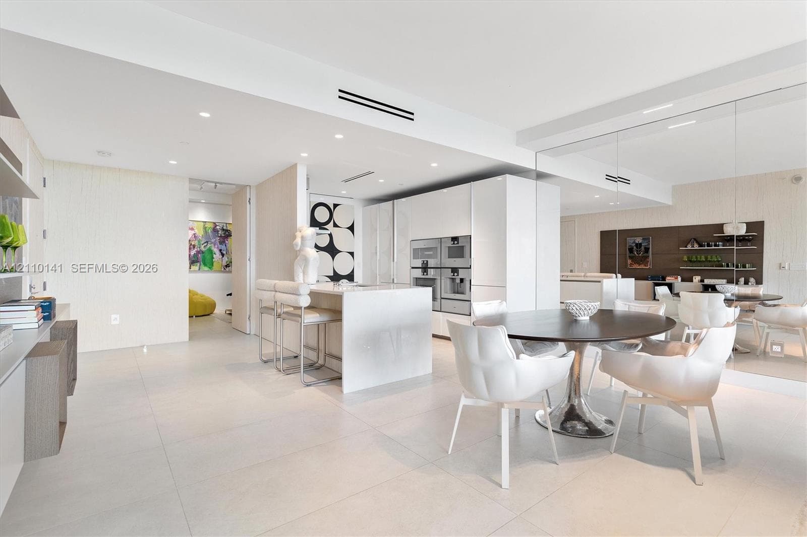 Contemporary kitchen featuring white slab-panel cabinetry, a central island with integrated stone waterfall-edge countertop, Large pantry