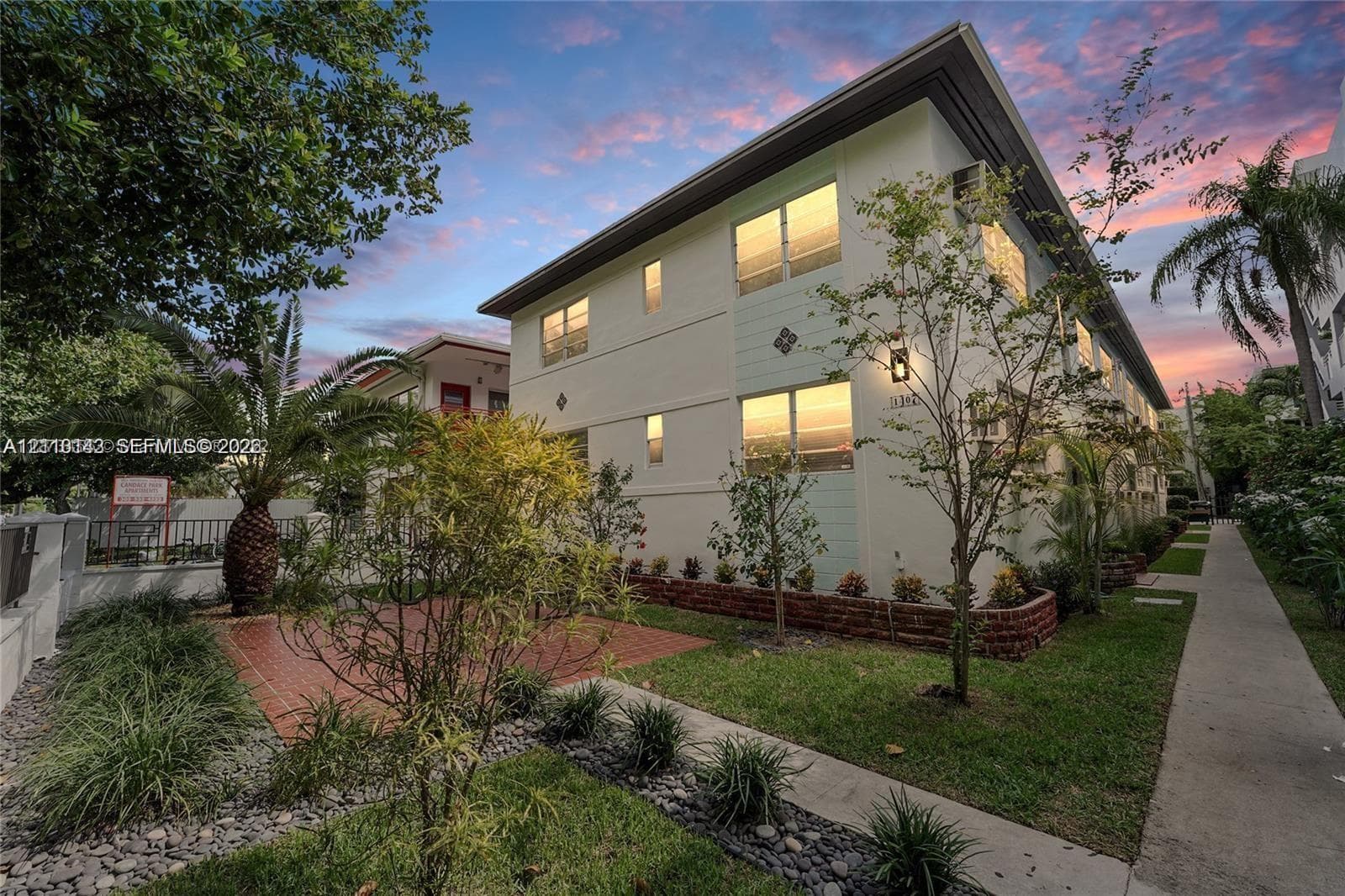 Multi-story exterior featuring light-toned stucco facade, paved brick patio, and manicured landscaping with stone border accents