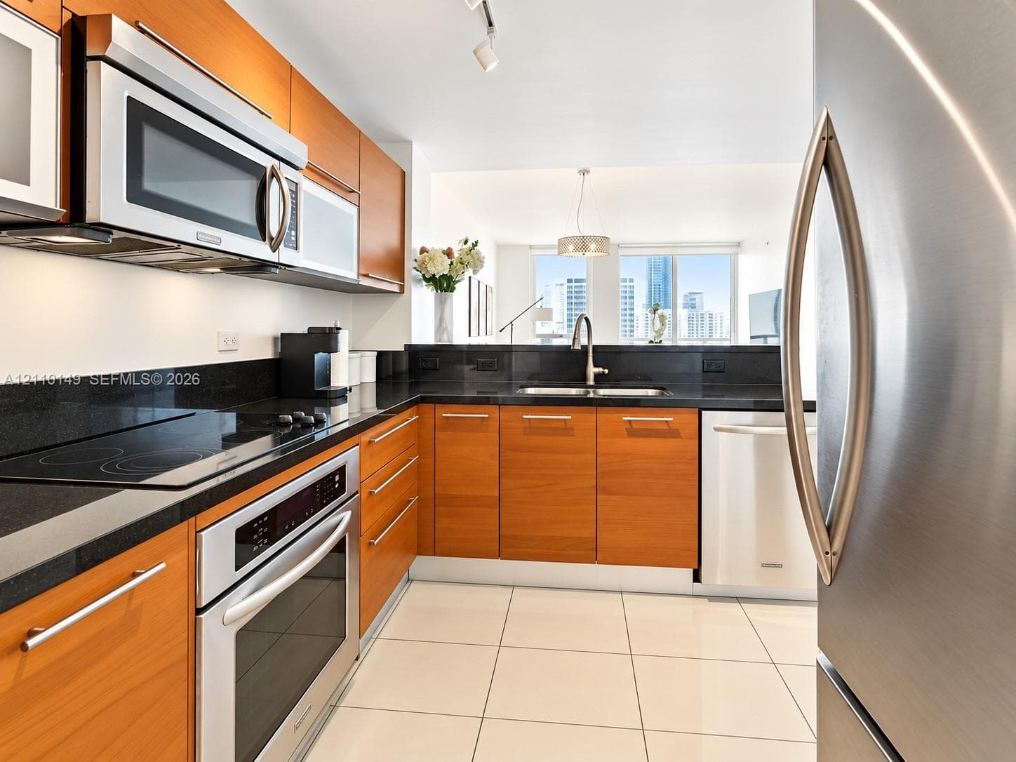 Kitchen featuring wood-finish cabinetry, dark stone countertops, stainless steel appliances, and large-format tile flooring