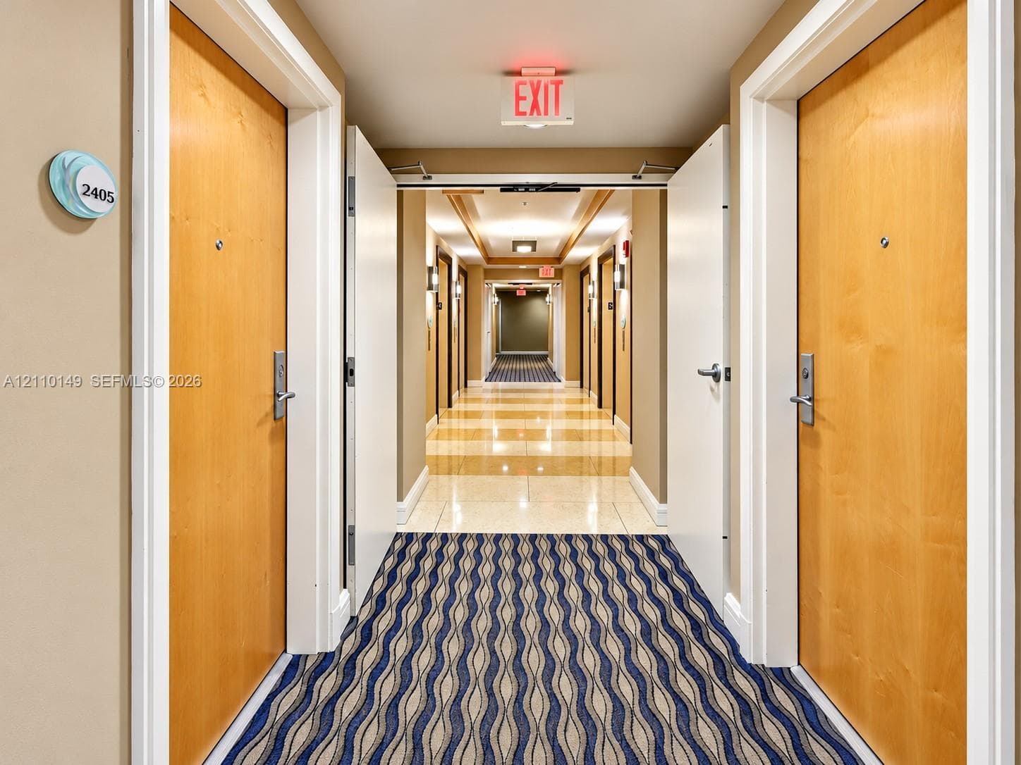 Common area hallway featuring patterned carpet, light-tone tile flooring, and wood-finish doors with metal hardware